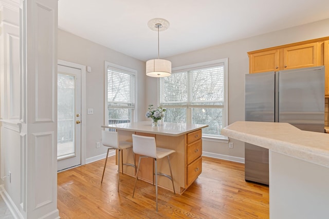 kitchen featuring light wood-type flooring, a healthy amount of sunlight, light countertops, and stainless steel refrigerator