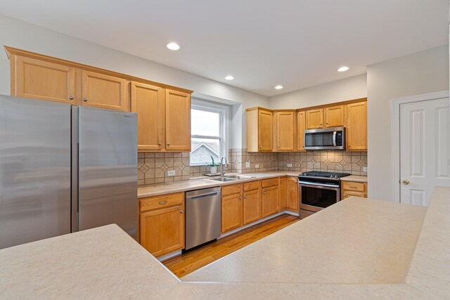 kitchen featuring light wood finished floors, stainless steel appliances, light countertops, decorative backsplash, and a sink