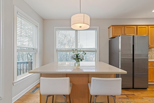 kitchen with visible vents, baseboards, light wood-style flooring, a breakfast bar area, and freestanding refrigerator