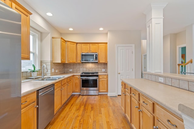 kitchen with tasteful backsplash, light wood-style flooring, appliances with stainless steel finishes, light countertops, and a sink