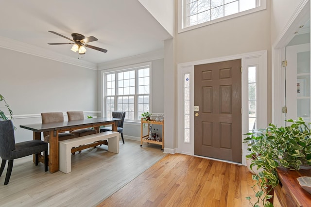 foyer featuring a ceiling fan, crown molding, light wood-style flooring, and baseboards