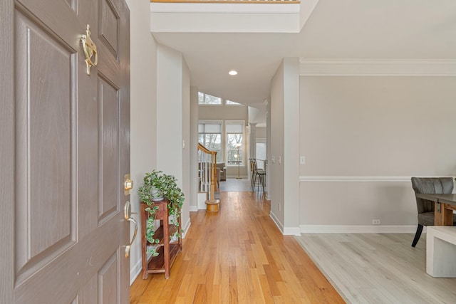 entryway featuring light wood-style floors, ornamental molding, vaulted ceiling, baseboards, and stairs