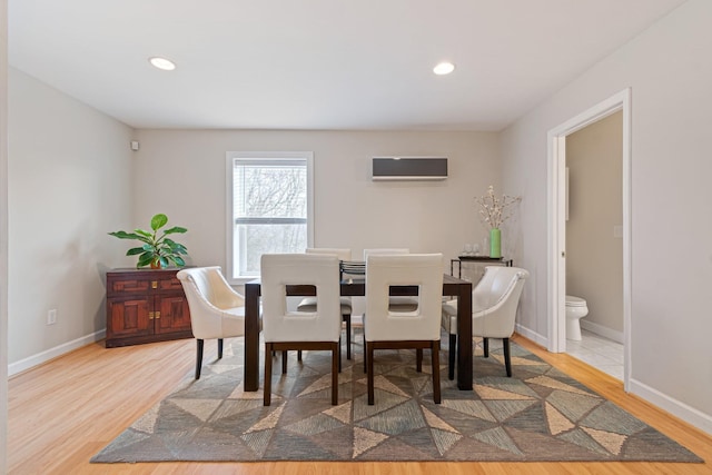 dining room with a wall unit AC, baseboards, and wood finished floors