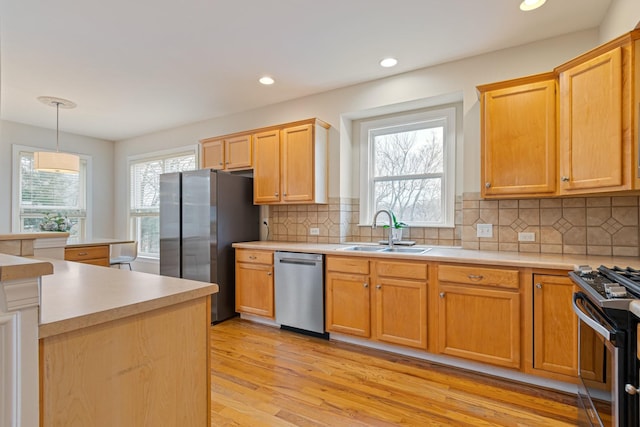 kitchen featuring a sink, light wood-style floors, light countertops, appliances with stainless steel finishes, and plenty of natural light