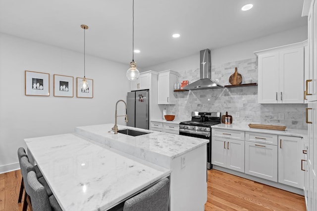 kitchen with wall chimney exhaust hood, light wood-style floors, a sink, and stainless steel appliances