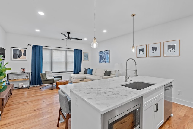 kitchen featuring light wood-style flooring, stainless steel appliances, a sink, white cabinetry, and pendant lighting