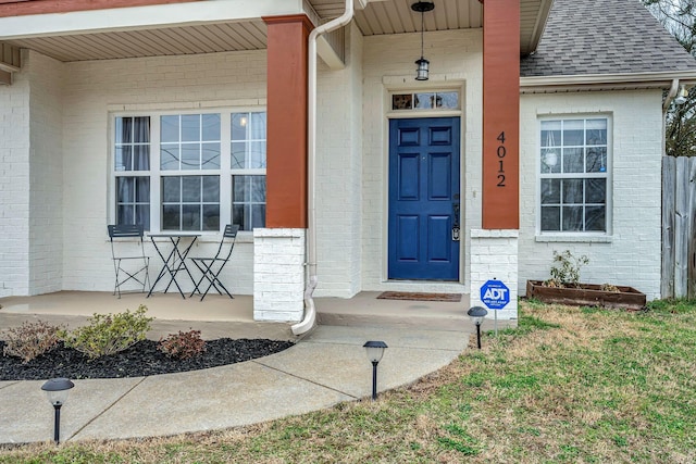 entrance to property with a shingled roof, brick siding, and a porch