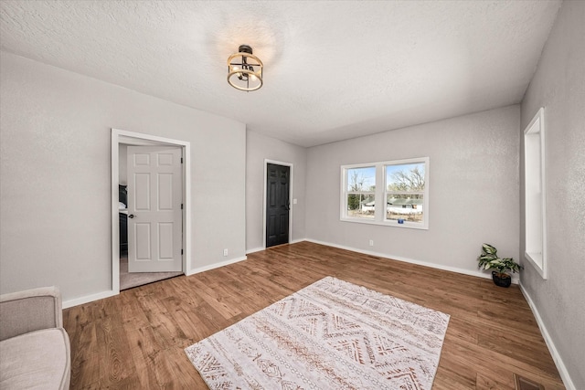 living area featuring visible vents, a textured ceiling, baseboards, and wood finished floors