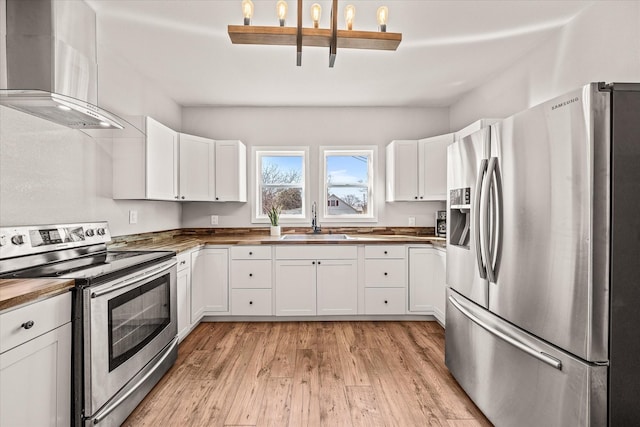 kitchen featuring white cabinets, wall chimney exhaust hood, stainless steel appliances, light wood-style floors, and a sink