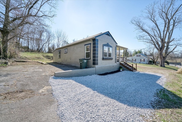 view of side of home with gravel driveway and stucco siding