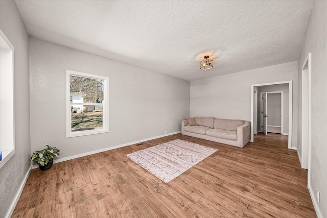 unfurnished living room with a textured ceiling, baseboards, and wood finished floors