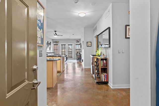 hallway with concrete flooring, visible vents, and baseboards