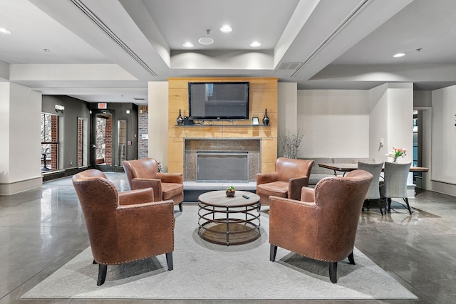 living room featuring a tray ceiling, recessed lighting, a fireplace with raised hearth, finished concrete floors, and baseboards