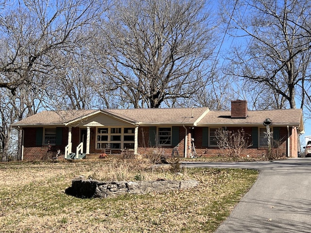 ranch-style house with brick siding, a chimney, a porch, and aphalt driveway