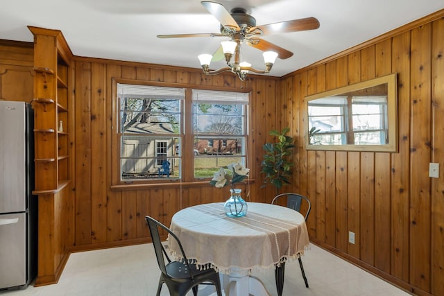 dining space with light floors, baseboards, a ceiling fan, and wood walls