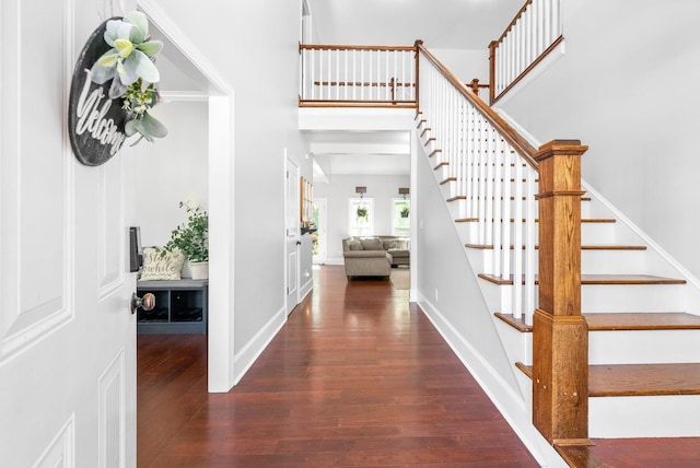 foyer with stairway, wood finished floors, a towering ceiling, and baseboards