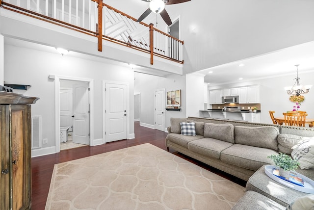 living room with a towering ceiling, baseboards, dark wood-style flooring, and ceiling fan with notable chandelier