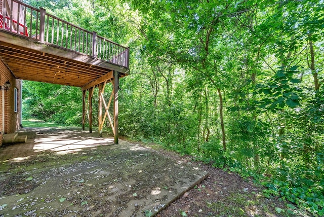 view of yard featuring a patio area, a wooden deck, and a forest view