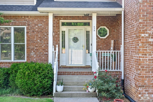 entrance to property with a shingled roof and brick siding