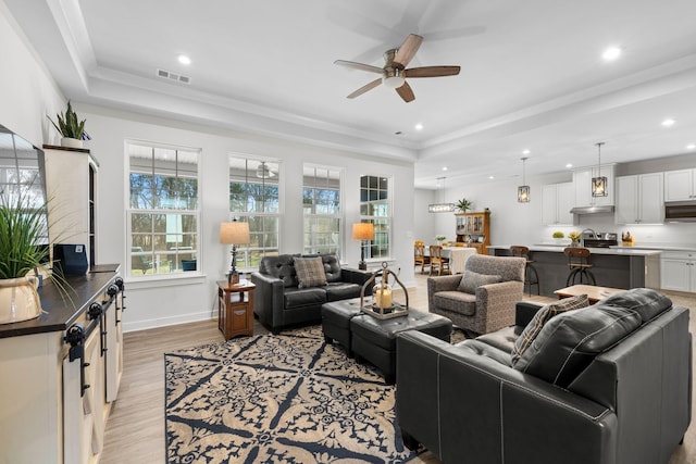 living room featuring light wood finished floors, visible vents, a tray ceiling, and baseboards