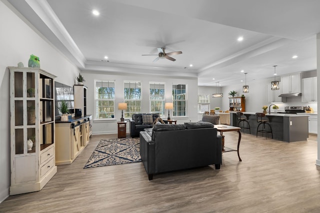 living area with crown molding, light wood finished floors, recessed lighting, a raised ceiling, and a ceiling fan