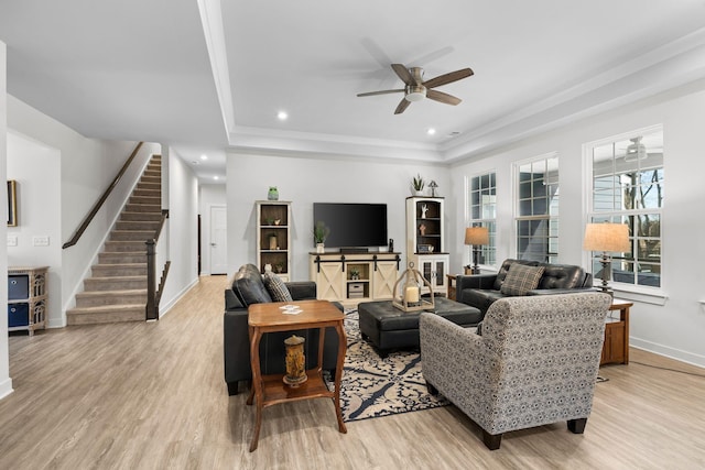 living area featuring stairway, light wood-type flooring, a raised ceiling, and baseboards