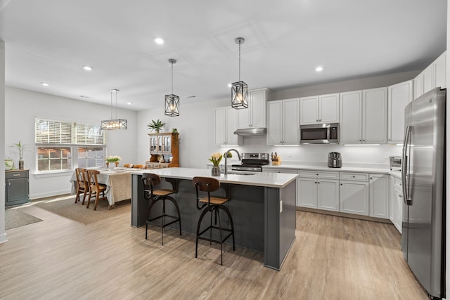 kitchen with stainless steel appliances, light countertops, under cabinet range hood, and light wood finished floors