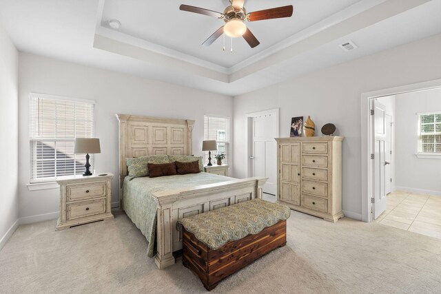 bedroom featuring light carpet, baseboards, a tray ceiling, and a ceiling fan