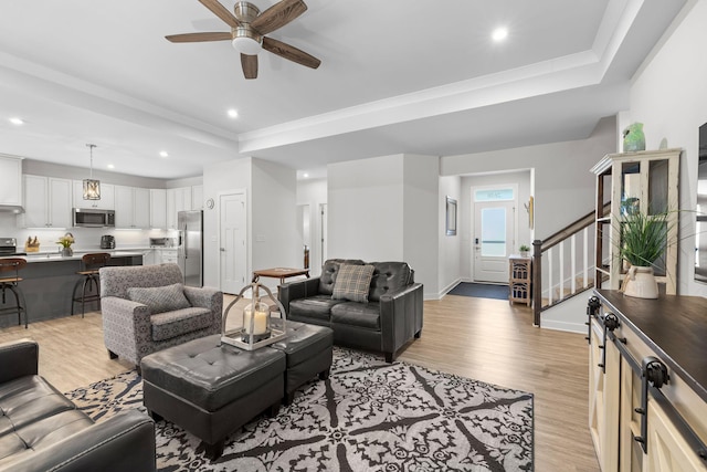 living area with stairs, a tray ceiling, light wood-type flooring, and recessed lighting