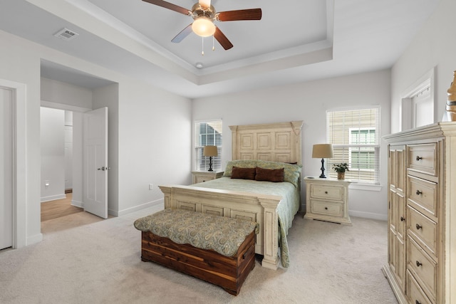 bedroom featuring light carpet, a tray ceiling, multiple windows, and visible vents