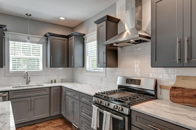 kitchen with light stone counters, stainless steel range with gas cooktop, tasteful backsplash, a sink, and wall chimney range hood