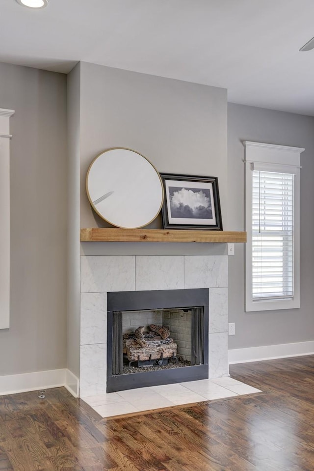 room details featuring baseboards, a tiled fireplace, and wood finished floors