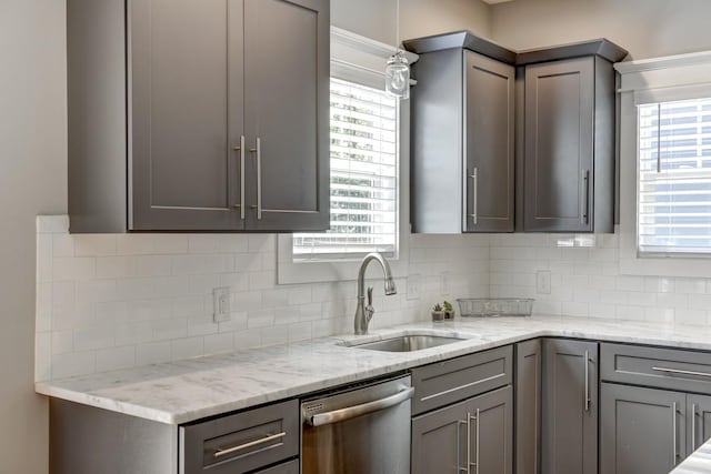 kitchen with light stone counters, gray cabinetry, dishwasher, and a sink