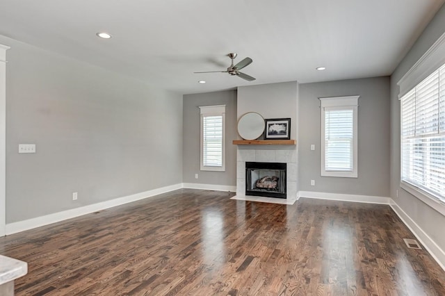 unfurnished living room featuring dark wood-style floors, a tiled fireplace, visible vents, and a healthy amount of sunlight