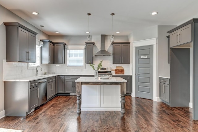 kitchen with light stone counters, dark wood-type flooring, a sink, wall chimney range hood, and appliances with stainless steel finishes