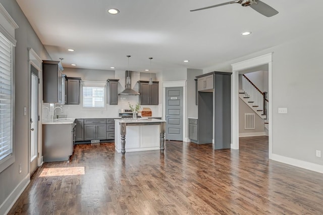 kitchen with a center island, dark wood-style flooring, visible vents, and wall chimney range hood