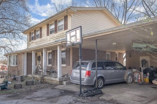 view of front of home featuring an attached carport, covered porch, brick siding, and driveway