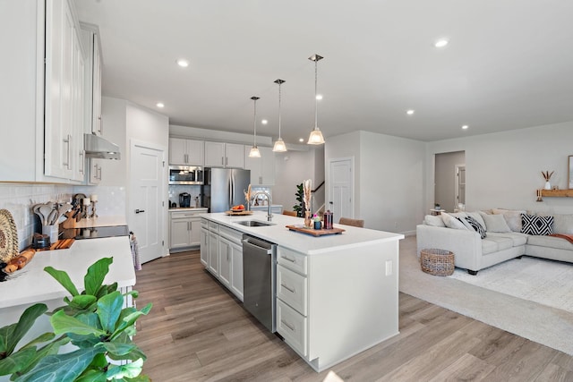 kitchen featuring under cabinet range hood, stainless steel appliances, a sink, open floor plan, and light wood finished floors