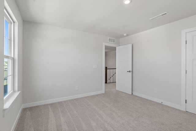 empty room with light carpet, plenty of natural light, and visible vents