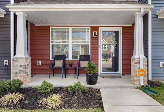 doorway to property featuring a porch and a shingled roof