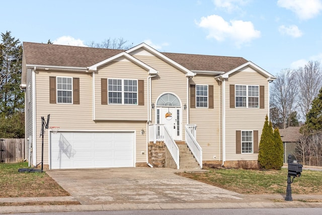 split foyer home featuring concrete driveway, roof with shingles, an attached garage, and fence