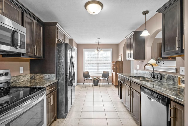 kitchen featuring dark stone countertops, stainless steel appliances, dark brown cabinets, a sink, and light tile patterned flooring