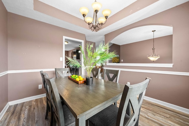 dining room with a tray ceiling, an inviting chandelier, baseboards, and wood finished floors