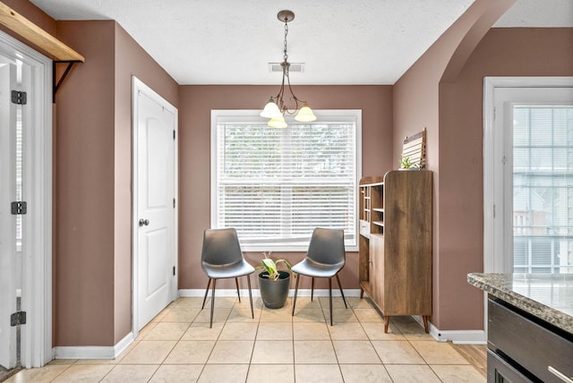 sitting room with arched walkways, light tile patterned floors, an inviting chandelier, a textured ceiling, and baseboards