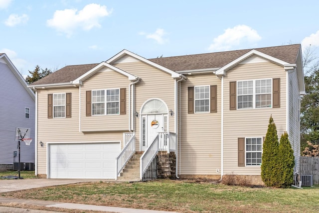 raised ranch featuring driveway, an attached garage, a shingled roof, and a front yard