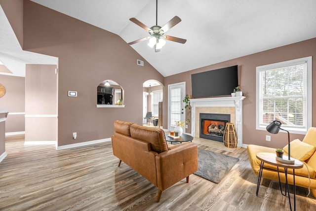 living area with ceiling fan, wood finished floors, visible vents, baseboards, and a tiled fireplace