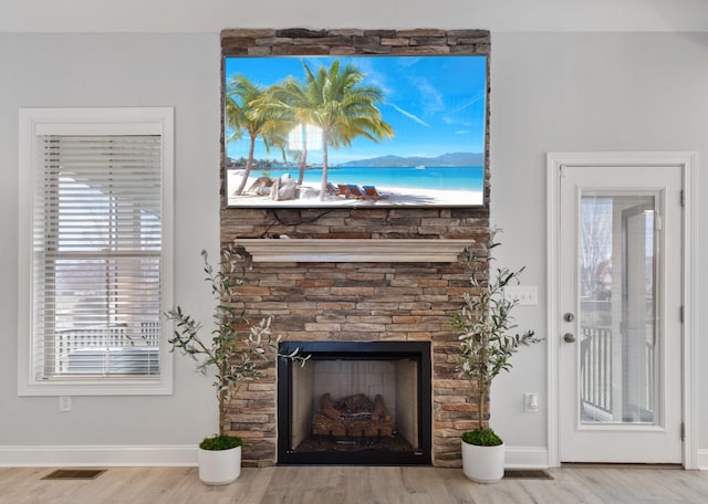 room details with visible vents, baseboards, wood finished floors, and a stone fireplace