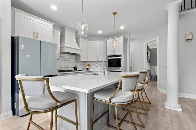 kitchen with tasteful backsplash, custom exhaust hood, stainless steel appliances, ornate columns, and a sink