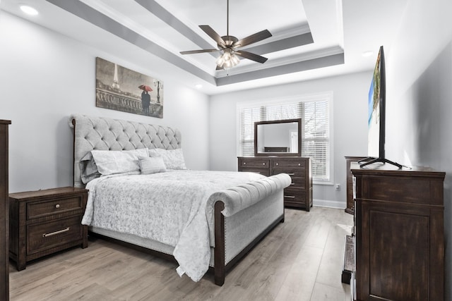 bedroom featuring light wood finished floors, baseboards, a raised ceiling, a ceiling fan, and ornamental molding