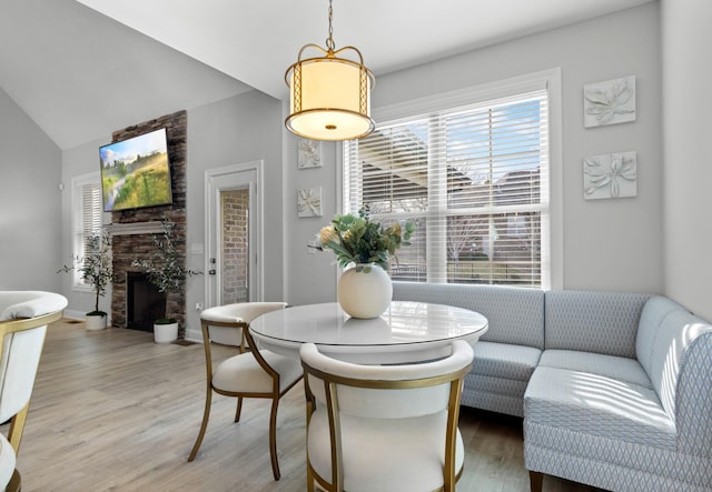 dining area with light wood finished floors, a stone fireplace, vaulted ceiling, and a wealth of natural light